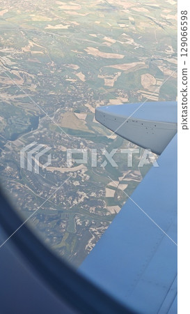 View from airplane window showing patchwork fields and landscapes far below the wing 129066598