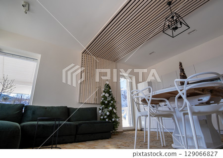 Interior of modern spacious kitchen with white walls, decorative wooden elements, contemporary furniture and big soft couch. 129066827