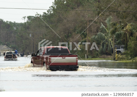 Hurricane flooded street with moving cars in surrounded with water Florida residential area. Consequences of natural disaster Hurricane flooded street with moving cars in surrounded with water Florida residential area. Consequences of natural disaster 129066857