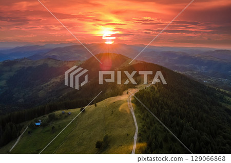 Hikers shelter on mountainside. Beautiful nature landscape. Aerial view of colorful sunset in wild mountains. Dark pine forest illuminated with bright setting sun Hikers shelter on mountainside. Beautiful nature landscape. Aerial view of colorful sunset in wild mountains. Dark pine forest illuminated with bright setting sun 129066868