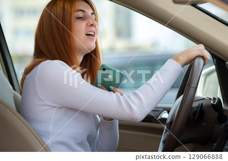Happy redhead girl talking on her mobile phone behind the wheel driving a car. Happy redhead girl talking on her mobile phone behind the wheel driving a car. 129066888