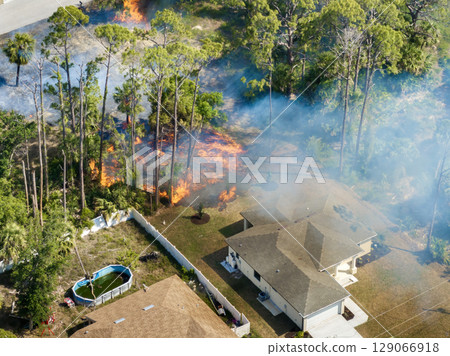 Flames from wildfire approach residential neighborhood in Florida with dense forest ablaze and smoke drifting over homes 129066918
