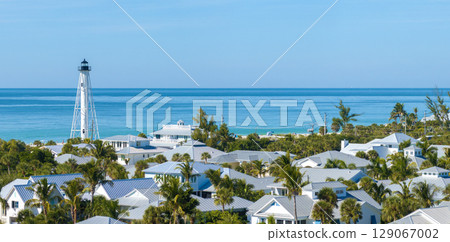 Expensive mansions between green palm trees in island small town Boca Grande in southwest Florida, USA. White lighthouse on sea shore for commercial vessels navigation 129067002