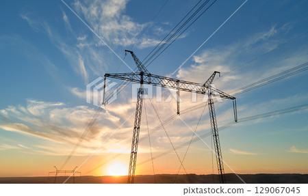 Dark silhouette of high voltage tower with electric power lines at sunrise. Transmission of electric energy concept 129067045
