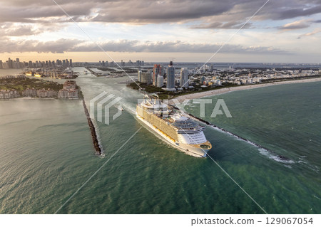 Cruise ship leaving Miami harbor main channel near South Beach. Luxurious hotels and apartment buildings on waterfront and high skyscrapers of downtown district in distance 129067054