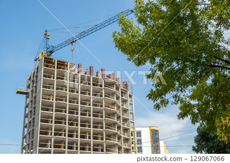 Concrete frame of tall apartment building under construction and tower crane in a city. 129067066