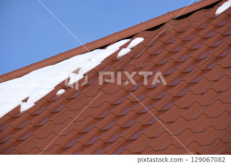 Closeup of house roof top covered with snow in cold winter. Tiled covering of building in wintertime weather 129067082