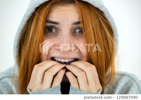 Close up portrait of scared young redhead woman wearing warm hoodie pullover. Close up portrait of scared young redhead woman wearing warm hoodie pullover. 129067090