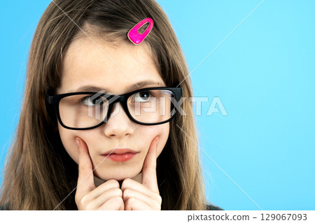 Close up portrait of a child school girl wearing looking glasses holding hand to her face thinking about something isolated on blue background. 129067093