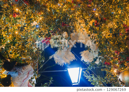 A decorated archway in London features greenery, fairy lights, and red and gold ornaments. A street lamp illuminates the holiday display. A decorated archway in London features greenery, fairy lights, and red and gold ornaments. A street lamp illuminates the holiday display. 129067269