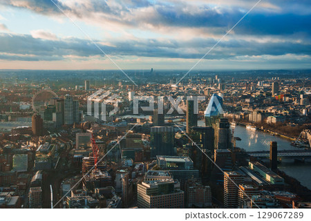 Aerial view of London featuring the London Eye, The Gherkin, and River Thames. Partly cloudy sky casts soft light over the festive cityscape. Aerial view of London featuring the London Eye, The Gherkin, and River Thames. Partly cloudy sky casts soft light over the festive cityscape. 129067289