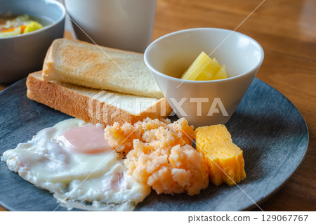 A mixed Japanese-Western breakfast featuring toast, fried eggs, mentaiko potatoes, and fruit. A mixed Japanese-Western breakfast featuring toast, fried eggs, mentaiko potatoes, and fruit. 129067767