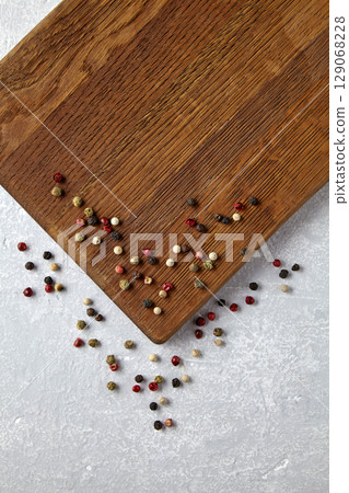 beige wooden cutting board with scattered colorful peppercorns top view. 129068228