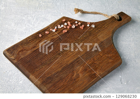 beige wooden cutting board with scattered colorful peppercorns on gray concrete table. 129068230
