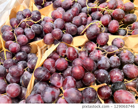 Vibrant purple grapes arranged in natural baskets at a bustling market Vibrant purple grapes arranged in natural baskets at a bustling market 129068746