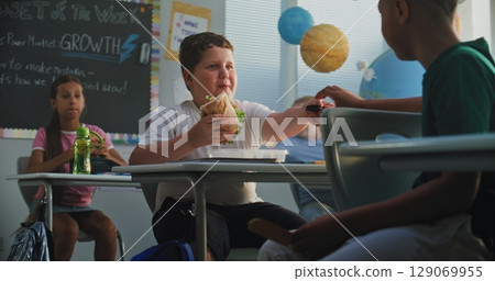 Primary School Boy Eating Sandwich from Lunch Box, Talking to Classmate. Diverse Kids Having Lunchtime 129069955