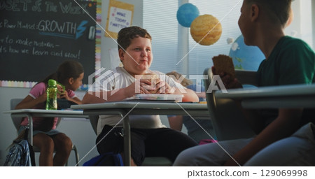 Primary School Boy Eating Sandwich from Lunch Box, Talking to Classmate. Diverse Kids Having Lunchtime 129069998