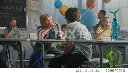 Primary School Children Sitting at the Desks, Eating Sandwiches from Lunch Boxes, Talking with Each Other Primary School Children Sitting at the Desks, Eating Sandwiches from Lunch Boxes, Talking with Each Other 129070010