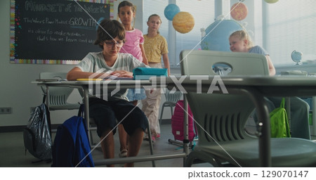 Depressed Primary School Boy Sitting at Desk While Classmates Abusing Him, Throwing Papers and Laughing Depressed Primary School Boy Sitting at Desk While Classmates Abusing Him, Throwing Papers and Laughing 129070147