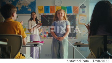 Shy Primary School Girl Showcasing Knowledge of Ecology in Front of Class and Teacher Shy Primary School Girl Showcasing Knowledge of Ecology in Front of Class and Teacher 129070158