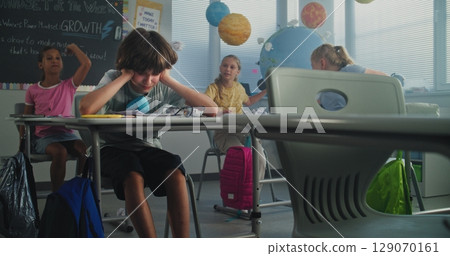 Depressed Primary School Boy Sitting at Desk While Classmates Abusing Him, Throwing Papers 129070161