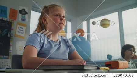 Stressed Primary School Girl Sitting at Desk While Classmates Abusing Her, Throwing Papers 129070165