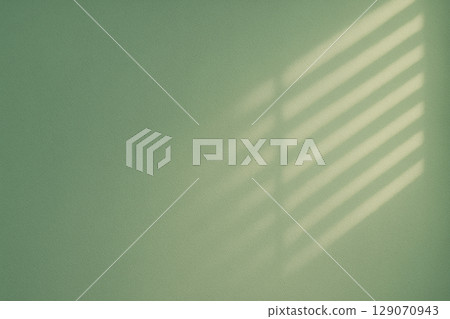 Shadows of blinds and gentle light shining on the green wall 129070943