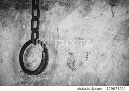 Monochrome shot of a rusty metal shackle (or handcuff) hanging on the wall. A shackle is a restraint, either physical or psychological, that restricts movement. 129071231