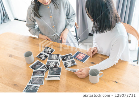 母親和女兒在客廳查看超音波影像,熱切地等待著孩子的出生 母親和女兒在客廳查看超音波影像,熱切地等待著孩子的出生 129072731