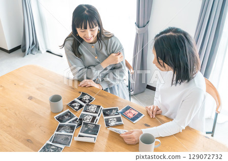 Mother and daughter looking at ultrasound images in the living room, eagerly awaiting the birth of their baby 129072732