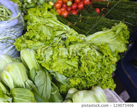 A vibrant market stall overflows with fresh vegetables, including leafy greens, tomatoes, and beans. A vibrant market stall overflows with fresh vegetables, including leafy greens, tomatoes, and beans. 129073406
