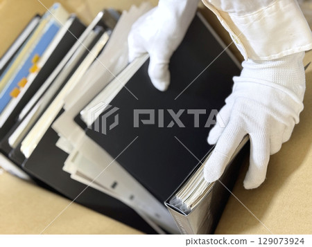 戴著白手套的手整理大量文件和文檔 戴著白手套的手整理大量文件和文檔 129073924