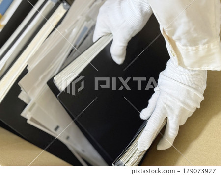 Hands in white gloves holding a file full of documents Hands in white gloves holding a file full of documents 129073927