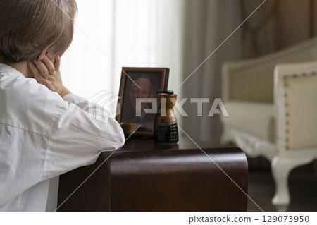 Alcohol and the elderly An elderly woman drinking in front of a portrait of the deceased 129073950