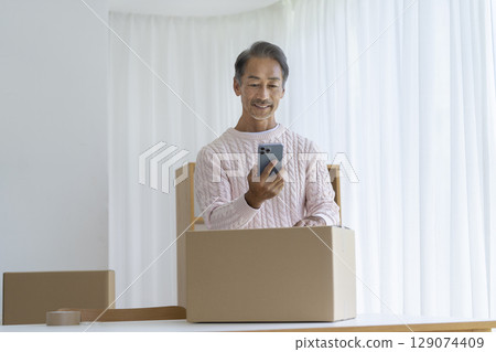 Senior man operating a smartphone Moving and decluttering image Senior man operating a smartphone Moving and decluttering image 129074409