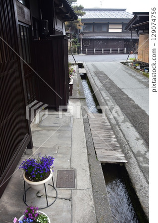 Spring in Gifu Prefecture, Japan. Old street in the center of Takayama city. Historic Japanese houses and small waterway. Beautiful potted plants on the roadside. 129074756