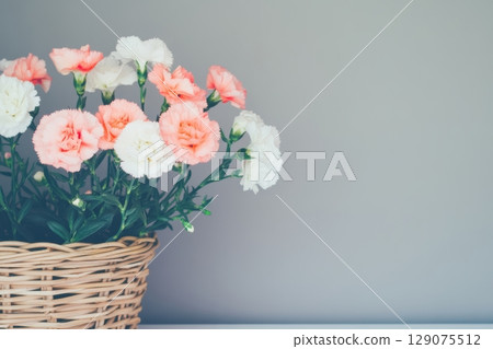 Colorful bouquet of carnations in a woven basket against a neutral wall background 129075512