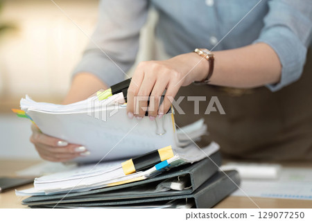 Organized Workspace. Businesswoman sorting through paperwork with colorful tabs. 129077250