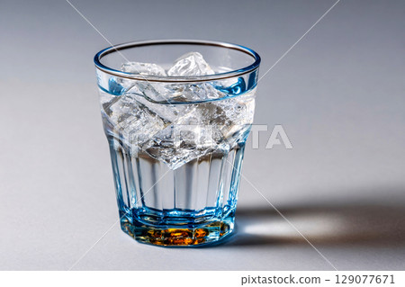 Glass of clear cold drink with ice cubes against a simple white backdrop 129077671