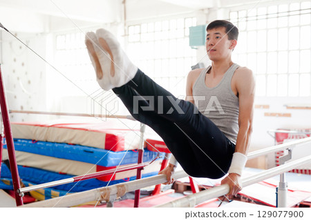 Focused gymnast practicing on parallel bars in gym 129077900