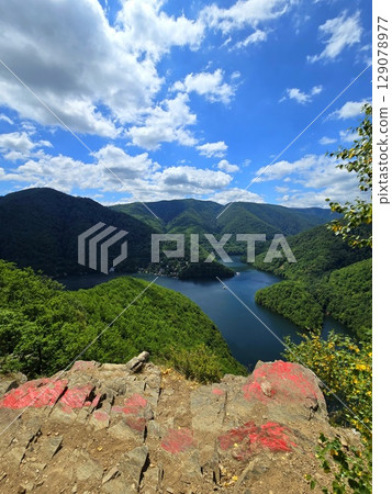 View from Piatra lui Lucaci over the Tarnita lake on a beautiful sunny summer day with blue sky and white clouds; red stone in foreground. Cluj, Romania 129078977