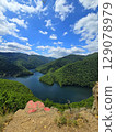 View from Piatra lui Lucaci over the Tarnita lake on a beautiful sunny summer day with blue sky and white clouds; red stone in foreground. Cluj, Romania 129078979