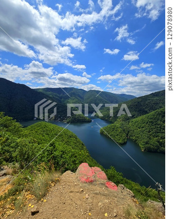 View from Piatra lui Lucaci over the Tarnita lake on a beautiful sunny summer day with blue sky and white clouds; red stone in foreground. Cluj, Romania 129078980