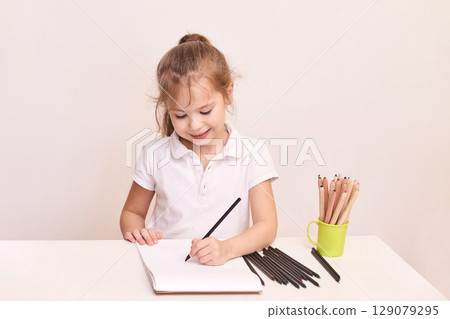 Caucasian young girl drawing with colored pencils at desk in white polo shirt 129079295