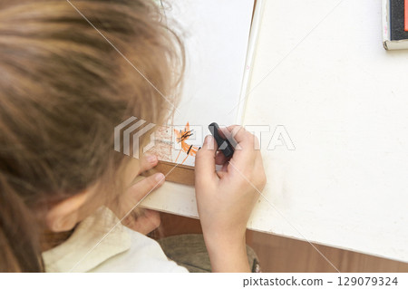 Young caucasian female child drawing with crayon on white paper at desk Young caucasian female child drawing with crayon on white paper at desk 129079324