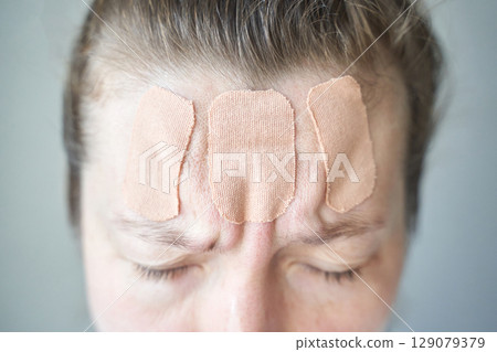 Female caucasian adult with forehead patches showing signs of discomfort 129079379