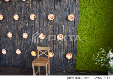 Wooden chair against rustic wall with industrial lights and green moss accent Wooden chair against rustic wall with industrial lights and green moss accent 129079413