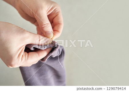 Hands mending gray sock with needle and thread crafting repair skillful sewing 129079414