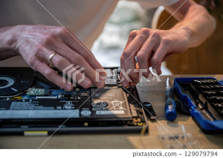 Man repairing laptop with tools on table, computer maintenance concept 129079794
