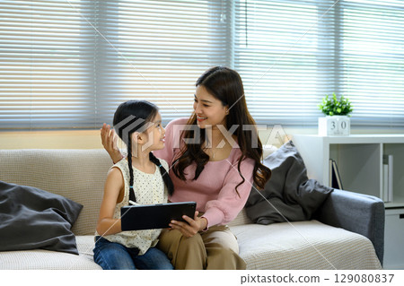 Happy mother and daughter sitting on sofa using a digital tablet together at home 129080837